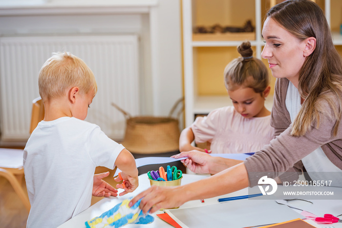 The teacher helping a child and they are working together making some paper crafts. Developing Fine motor skills for toddlers and preschoolers