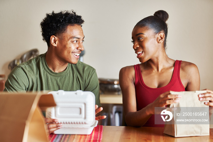 african american couple sitting at table looking at food delivery