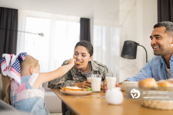 Daughter sharing cookie with mother having family breakfast