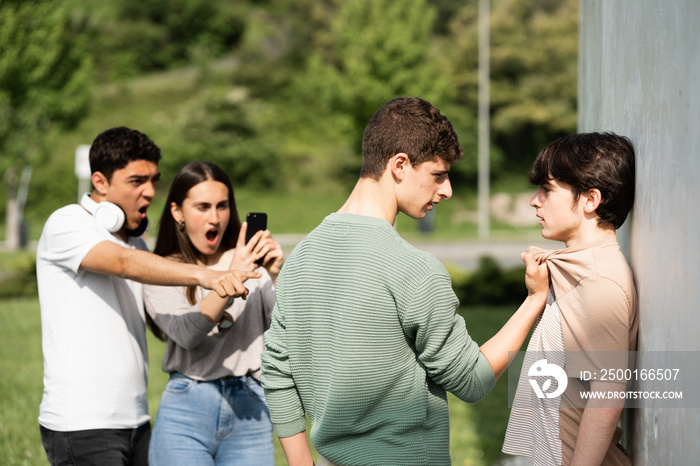 Teenager bully menacing boy while friends are recording. Bullying and violence at school concept