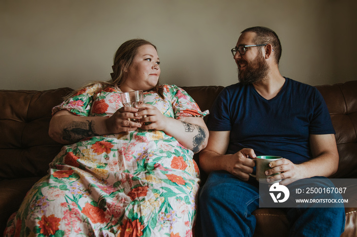 couple sits on sofa holding drinks