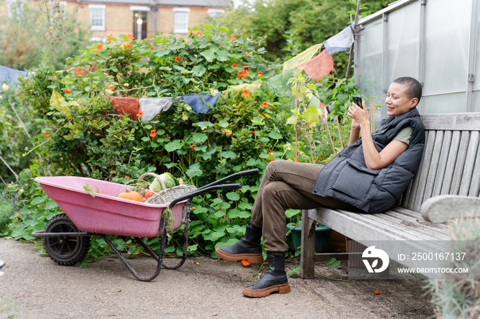 Smiling woman with smart phone in vegetable garden