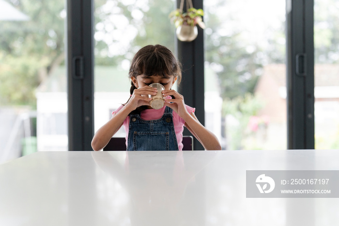 Little girl drinking from mug at table