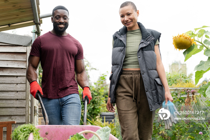 Smiling couple with vegetables in wheelbarrow in urban garden