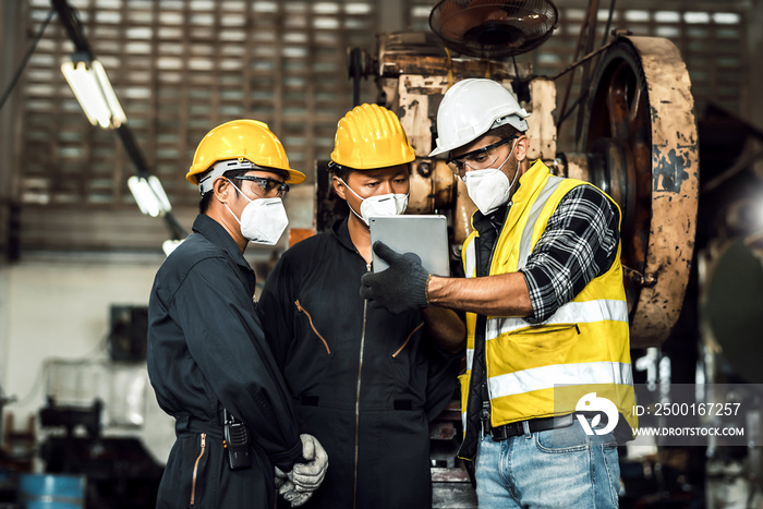 team engineer mechanic man wearing protective face mask and checking plan on tablet for maintenance metal machine at factory, teamwork concept