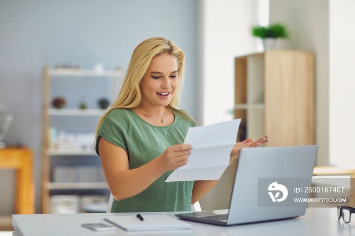 Happy woman sitting at desk at home reading notification paper letter about successful college or university admission, winning scholarship, loan approval, getting money refund, or salary increase