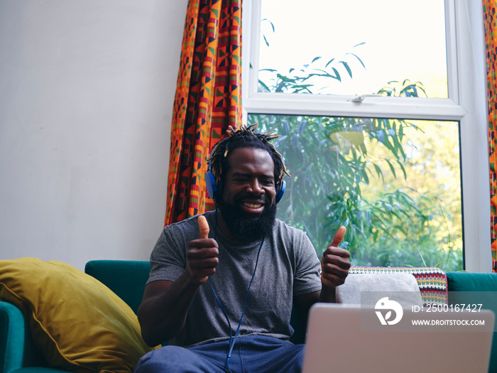 Man lying on sofa, listening to music from laptop