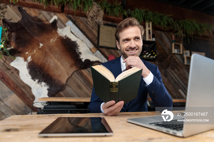 smiling businessman thinking and reading a book in a coffeeshop