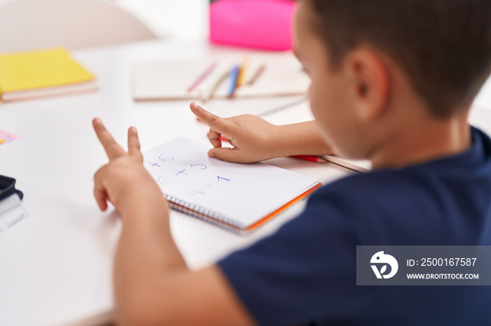 Adorable hispanic toddler doing mathematics exercise counting with fingers at classroom