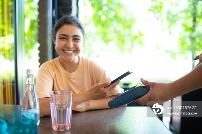 Indian Woman pay with mobile phone nfc contactless payment terminal in cafe bar