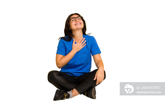 Young indian woman sitting on the floor cut out isolated laughs out loudly keeping hand on chest.