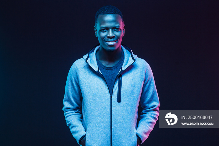 Dark neon portrait of smiling african man  wearing gray hoodie