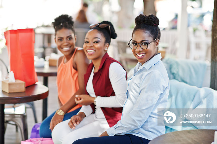 Three casual african american girls with colored shopping bags walking outdoor. Stylish black womans shopping.