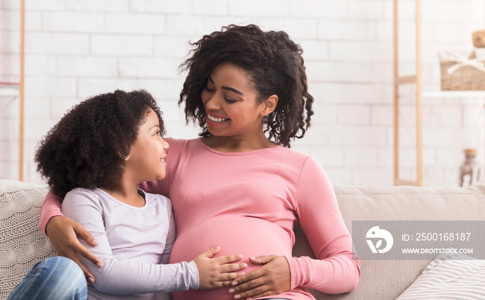 Joyful Pregnant Woman Embracing With Little Daughter On Sofa At Home