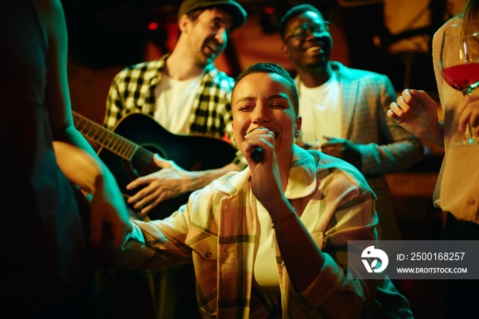 Young black woman sings while being with her friends on night party in bar.