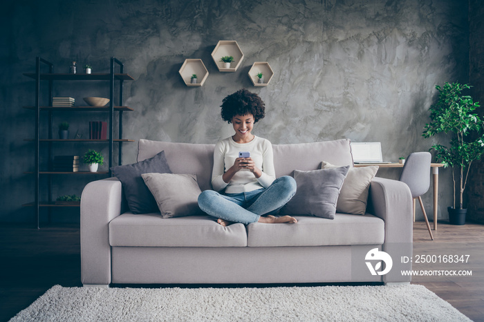 Photo of pretty dark skin curly lady homey domestic atmosphere texting telephone with friends reading instagram posts sitting comfy couch casual outfit flat loft indoors