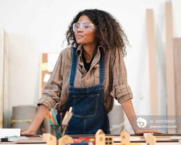 Portrait, female multiracial carpenter working in woodshop small business. Afro woman with goggles standing in DIY carpentry workshop with confidence. Empowerment joiner women in woodworking industry