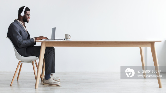 Black businessman in headphones making video call, sitting at desk, having web conference with customer at office