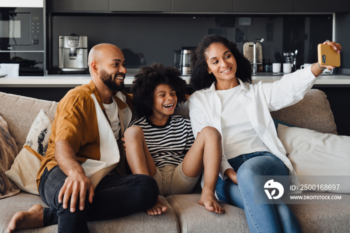 African american family taking selfie photo while sitting on sofa together at home