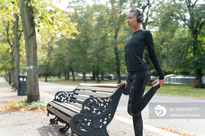 Woman in headphones and sports clothing stretching leg in park