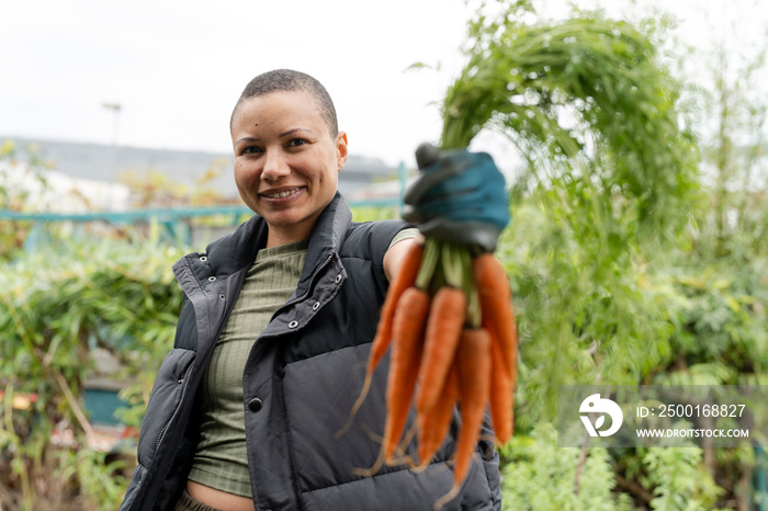 Portrait of smiling woman holding bunch of carrots in urban garden