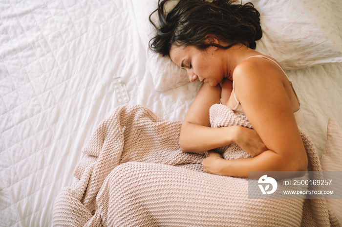 Young woman having stomachache lying on white bed