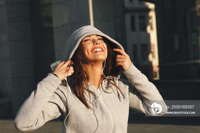 Young woman in gray hoodie enjoys music via headphones on the street