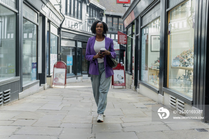 Confident woman walking with disposable cup in city