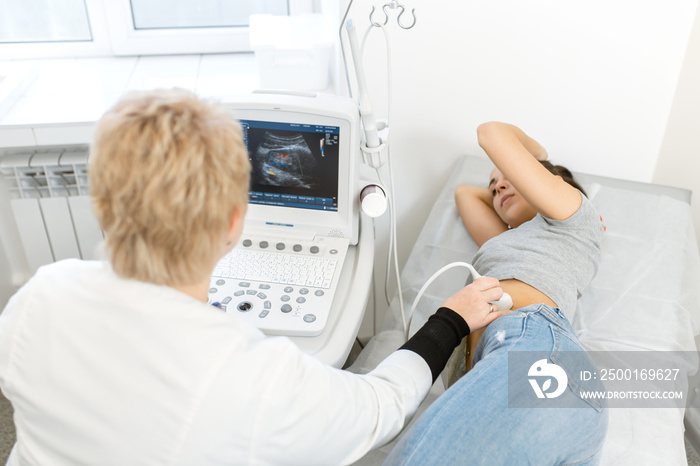 The doctor conducts an ultrasound diagnosis of the patients abdomen and internal organs. A girl lies on a couch in an ultrasound diagnostic room