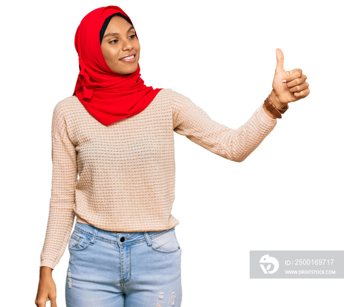 Young african american woman wearing traditional islamic hijab scarf looking proud, smiling doing thumbs up gesture to the side