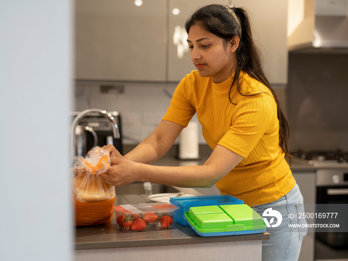 Young woman preparing lunch boxes in kitchen