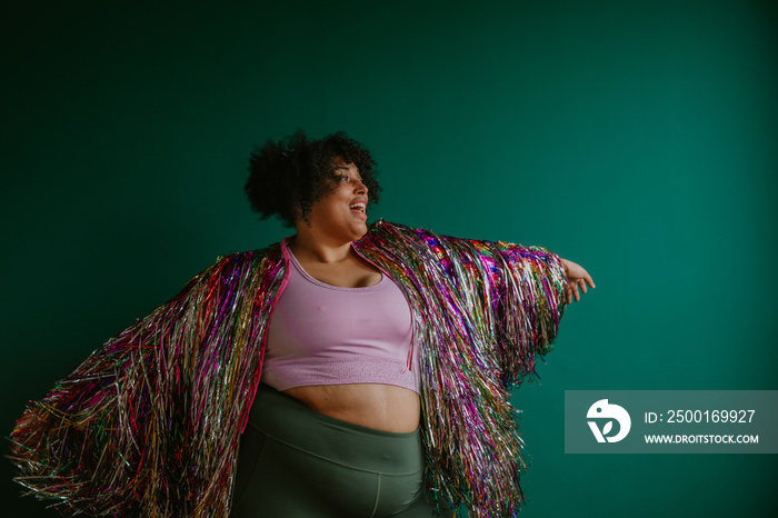 portrait of a plus size person dancing wearing rainbow tinsel jacket