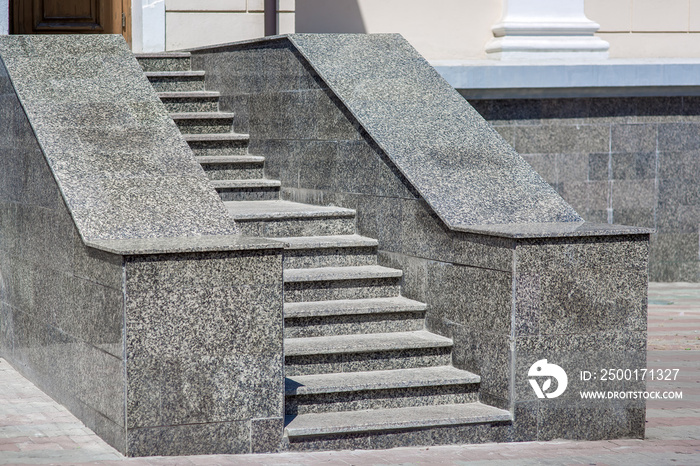 The gray granite steps of the staircase at the back entrance to the front-walled administrative capitol, a sunlit architectural building, nobody.