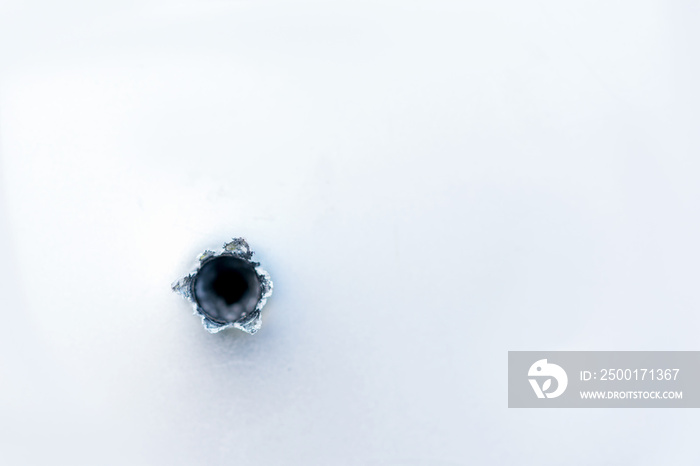 Bullet hole on the metal fragment from the white surface