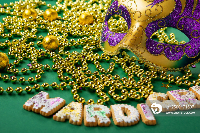 Mardi Gras King Cake Cookies, Carnival Masks, Gold Beads on Green Background.