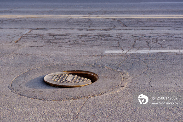 Broken iron manhole cover dangerously open in the middle of the street.