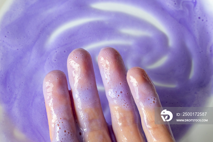 Shampoo or purple mask on a white background and on women’s hands. A remedy for blonde hair against yellowing.