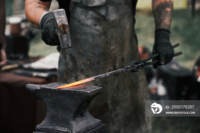 Blacksmith manually forging molten metal on anvil.