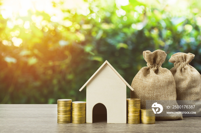 Saving money or property investment or buy a new home concept. A small house model with stack of coins and money bag on wood table. Depicts sustainable financial goal.