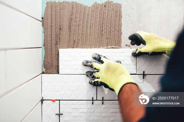 industrial construction worker installing small ceramic tiles on bathroom walls and applying mortar with trowel