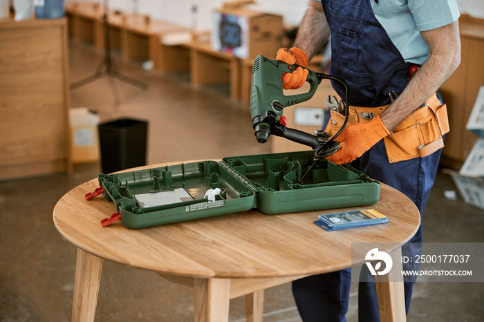 Male builder in gloves holding electric hammer drill