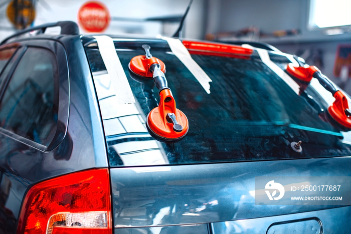 Automechanic is replacing windshield  of a car in auto service station garage.