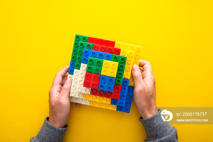 hand stacking up the colorful plastic block on yellow background