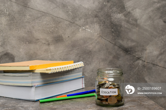 Coins in glass jar, book and pencil on marble table. Concept mone saving for education.