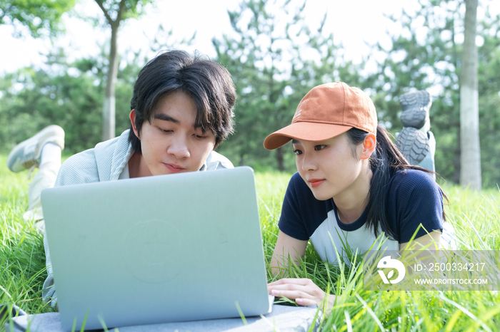 大学生情侣趴在草地上使用电脑