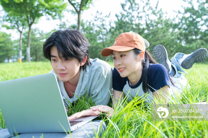 大学生情侣趴在草地上使用电脑