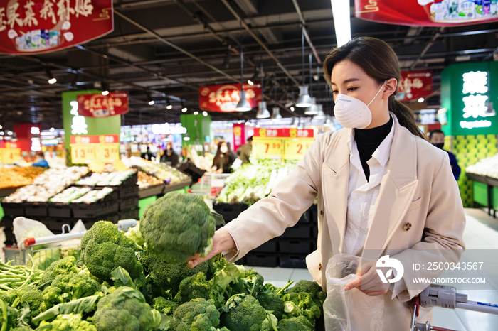 戴口罩的青年女人在超市挑选青菜