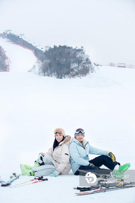 快乐的青年伴侣背靠背坐在雪地上