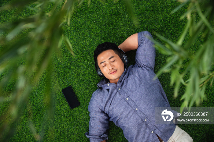 青年男人躺在草地上听音乐