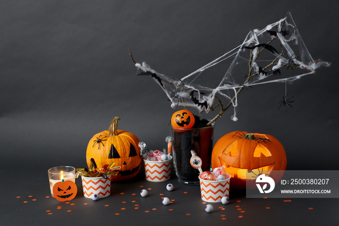 halloween and holiday decorations concept - jack-o-lantern or carved pumpkin, candies in paper cups,